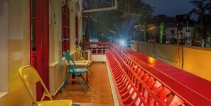 Un balcón con barandilla roja, sillas y vista a la calle por la noche.