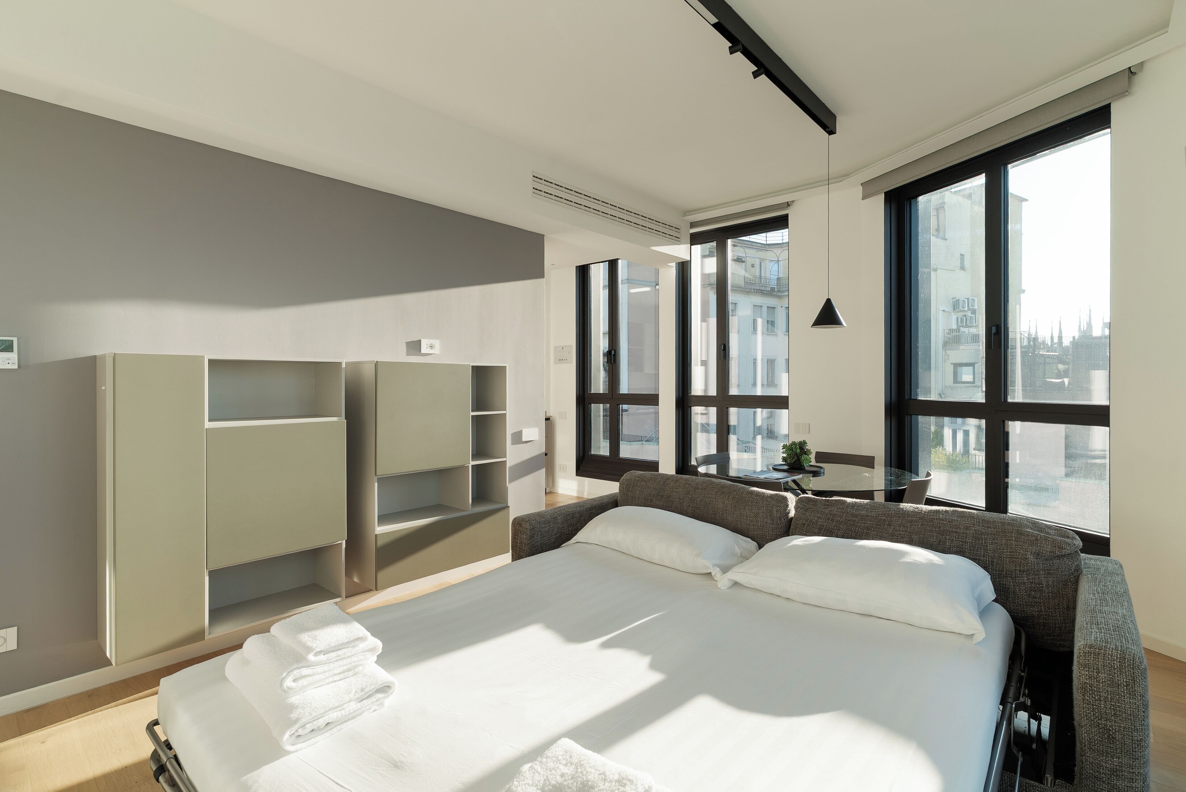 A modern hotel room with a large bed, built-in wardrobe, and a city view through large windows.