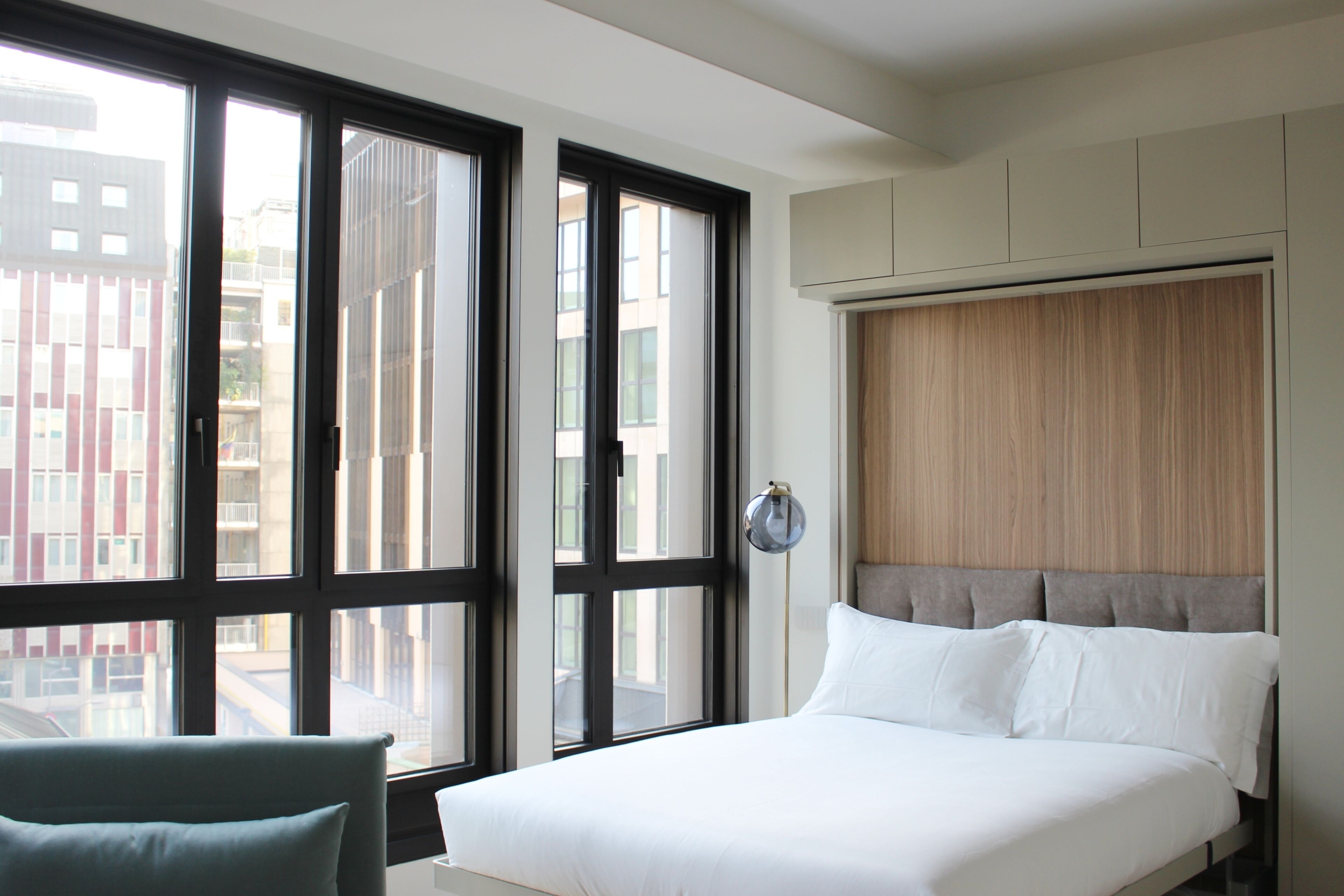 Une chambre d’hôtel moderne dotée d’un grand lit, offrant une vue imprenable grâce à de larges fenêtres du sol au plafond, et comprenant un placard intégré.