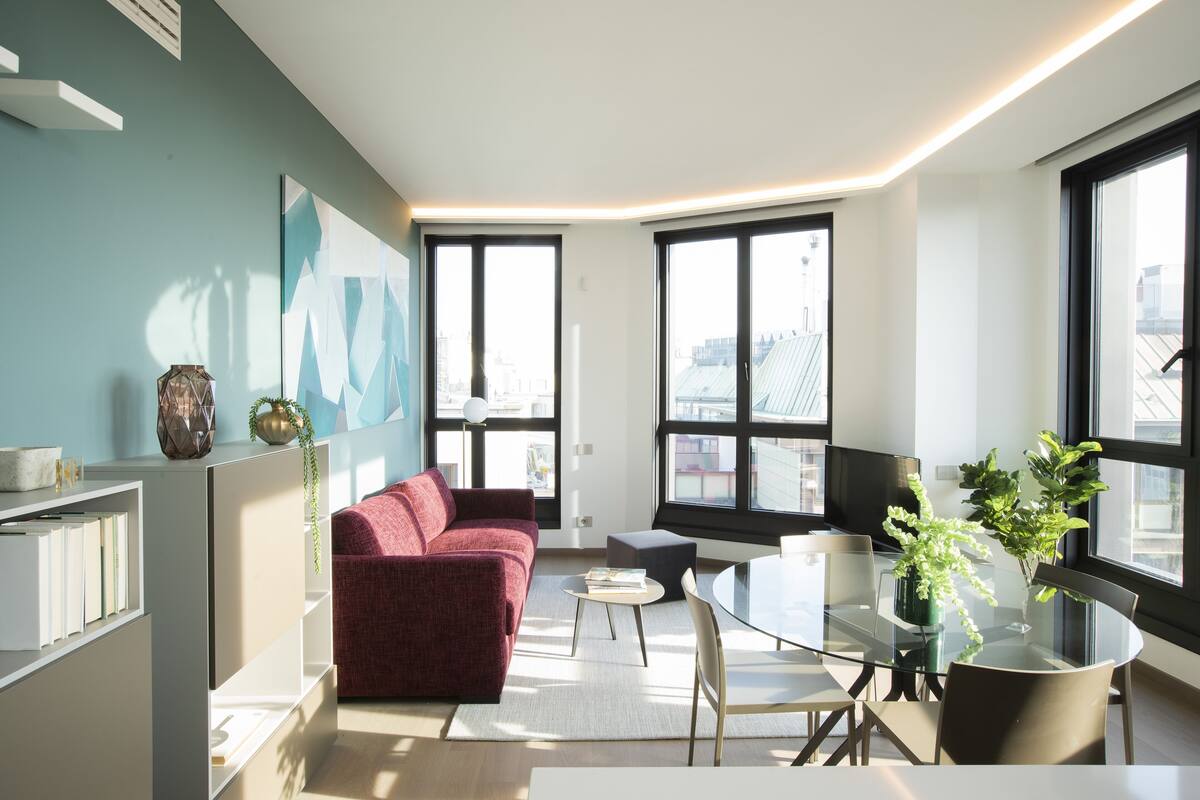 Un salon moderne avec un canapé rouge, une table en verre et une vue sur la ville grâce à de grandes fenêtres.