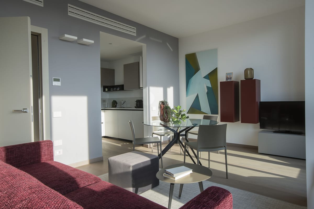 Un salon moderne avec un canapé rouge, une table à manger en verre et un téléviseur.