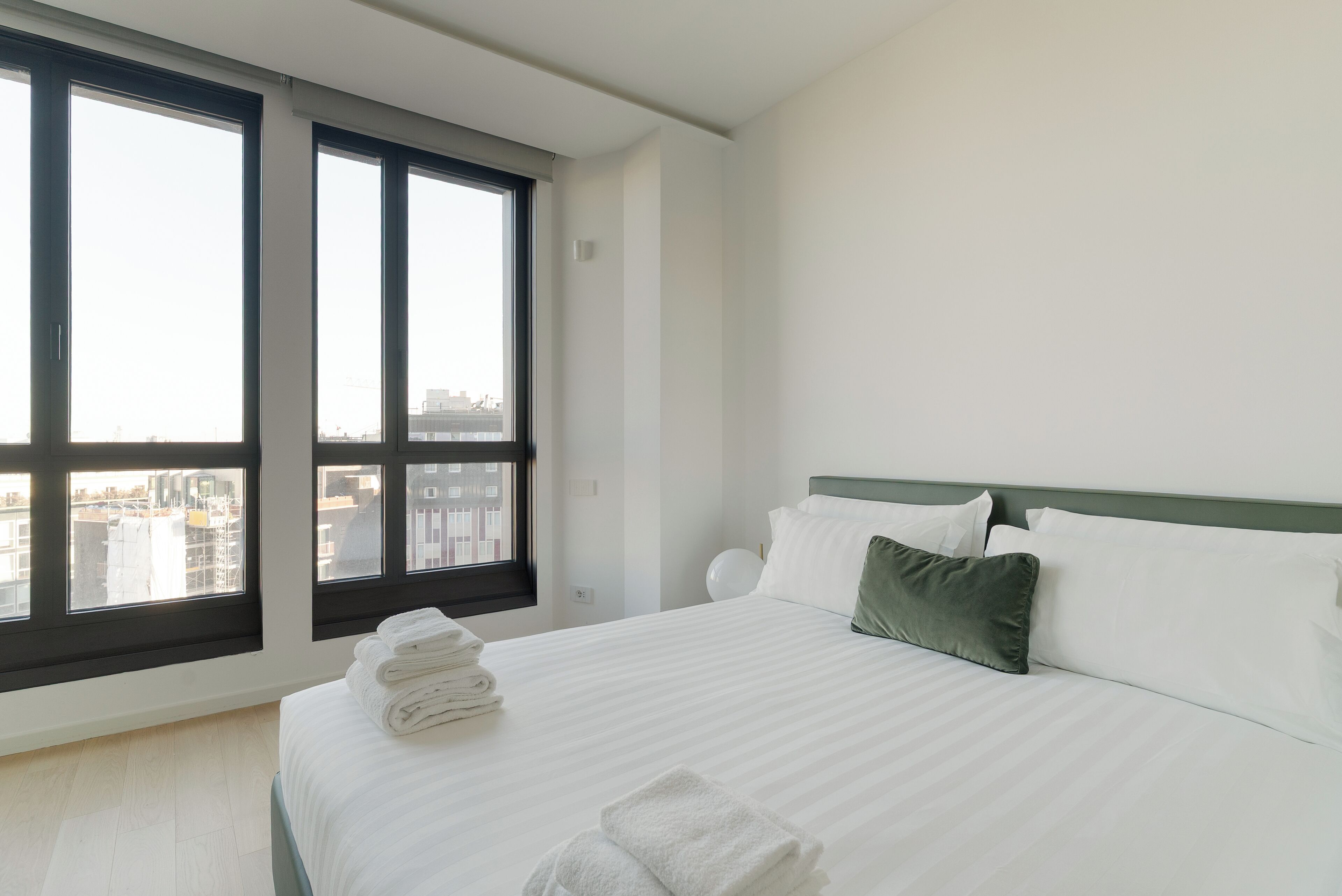 A hotel room with a large bed, a view of the city through floor-to-ceiling windows, and a neatly made bed with folded towels.