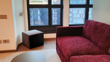 A modern living room with a red sofa, a small round table, and a view of buildings through large windows.