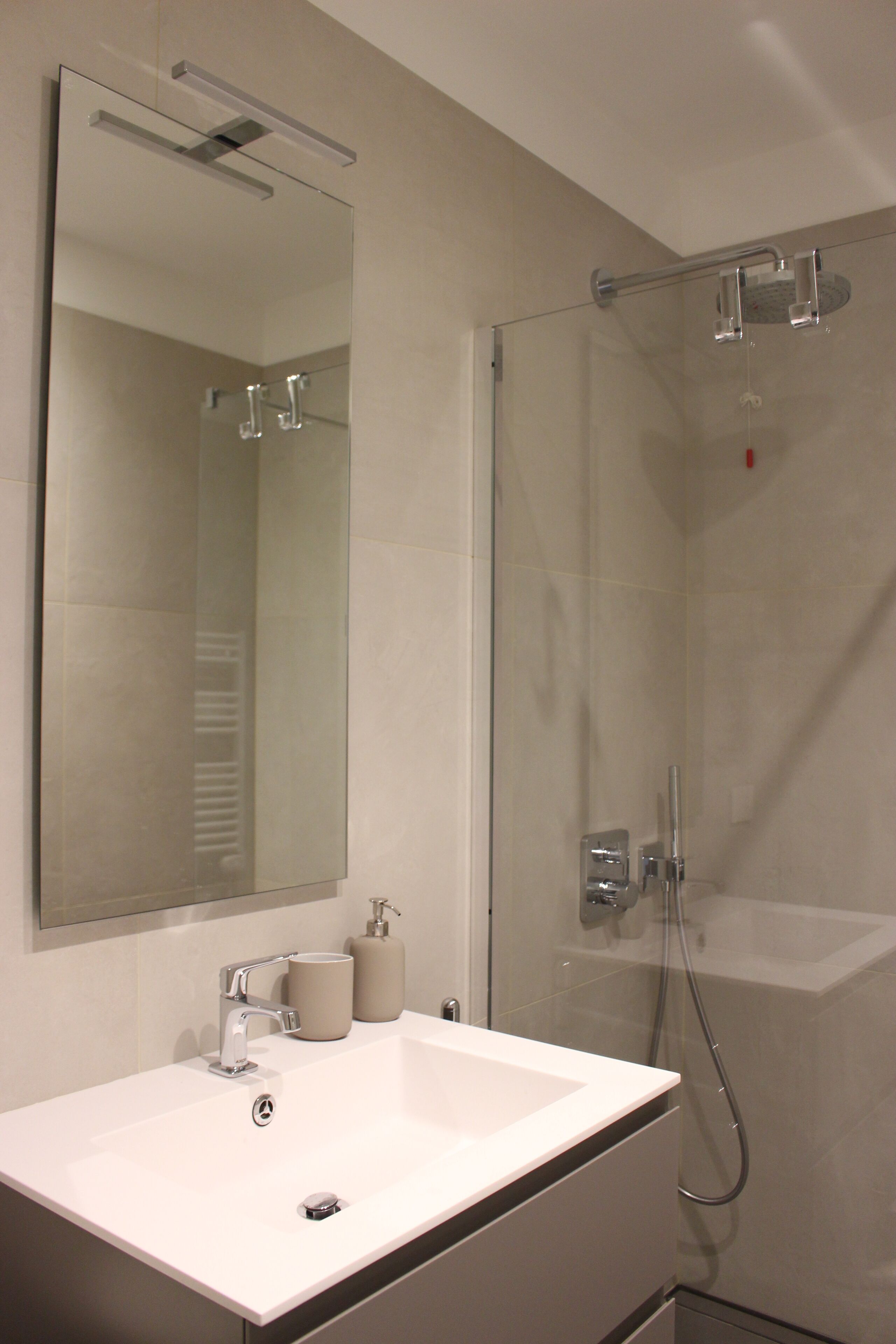 A modern bathroom with a white sink, a large mirror, and a glass-enclosed shower area.