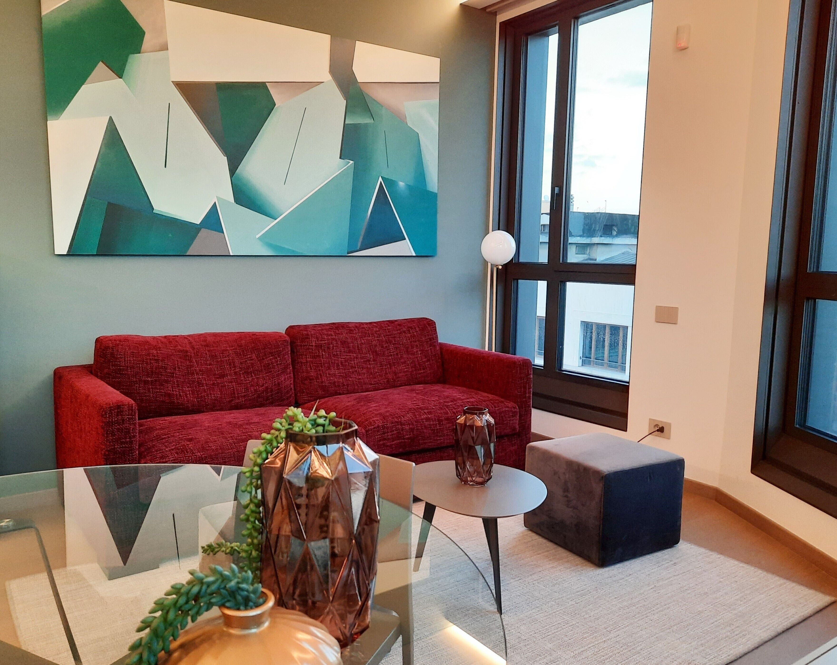 Una sala de estar moderna con un sofá rojo, una mesa de centro de cristal y un cuadro abstracto grande en la pared.