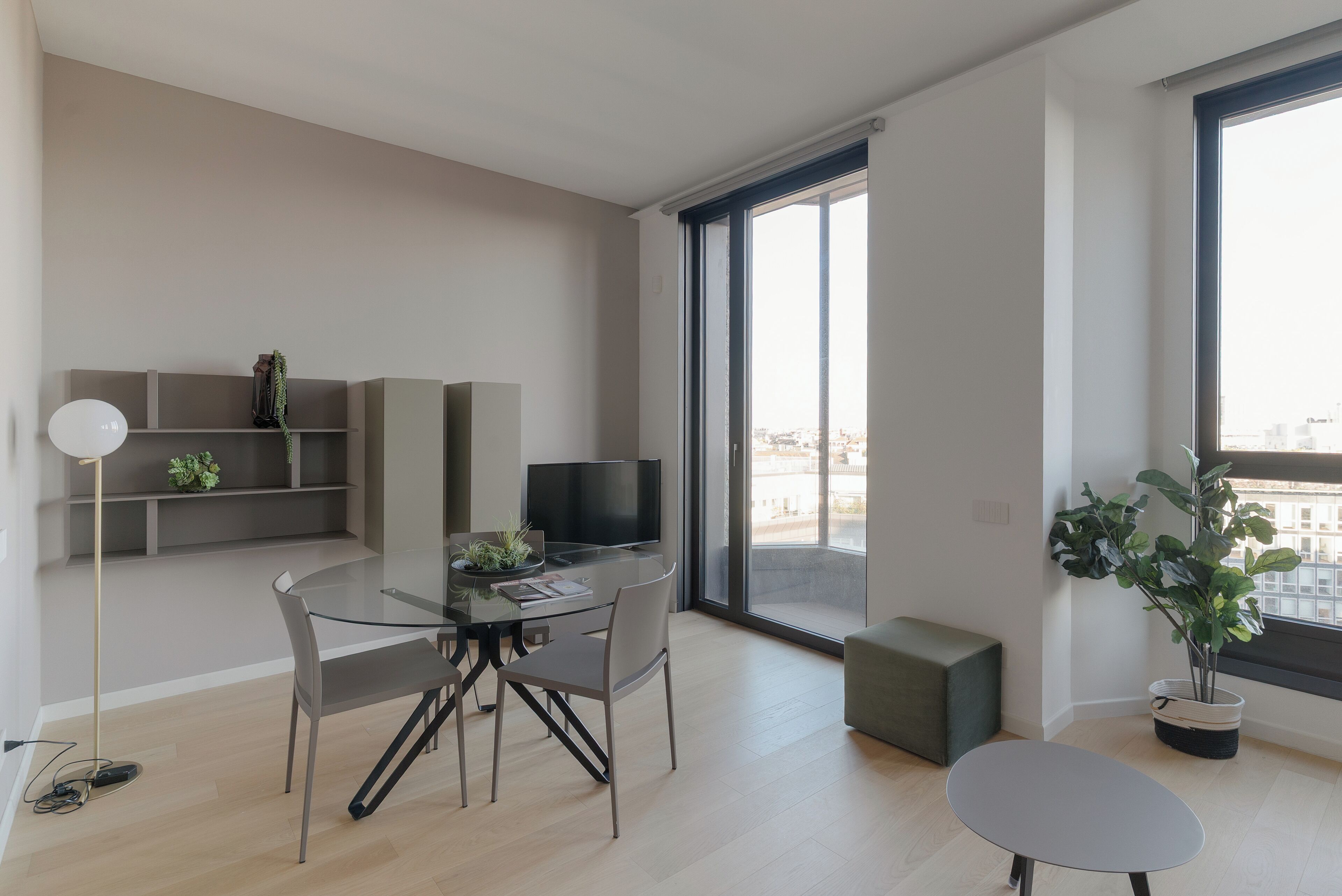 Una sala de estar moderna con una mesa de comedor de vidrio, un televisor de pantalla plana, un sofá y un ventanal con vistas a la ciudad.