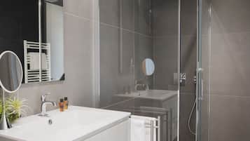 A modern bathroom with a glass-enclosed shower, a white vanity with a mirror, and a towel rack.