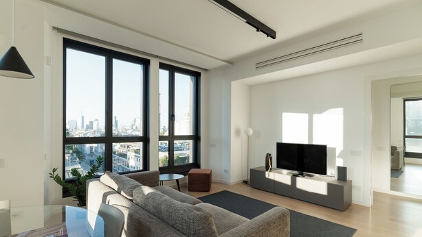 Una sala de estar moderna con un gran ventanal, un sofá, un televisor y una pequeña mesa.