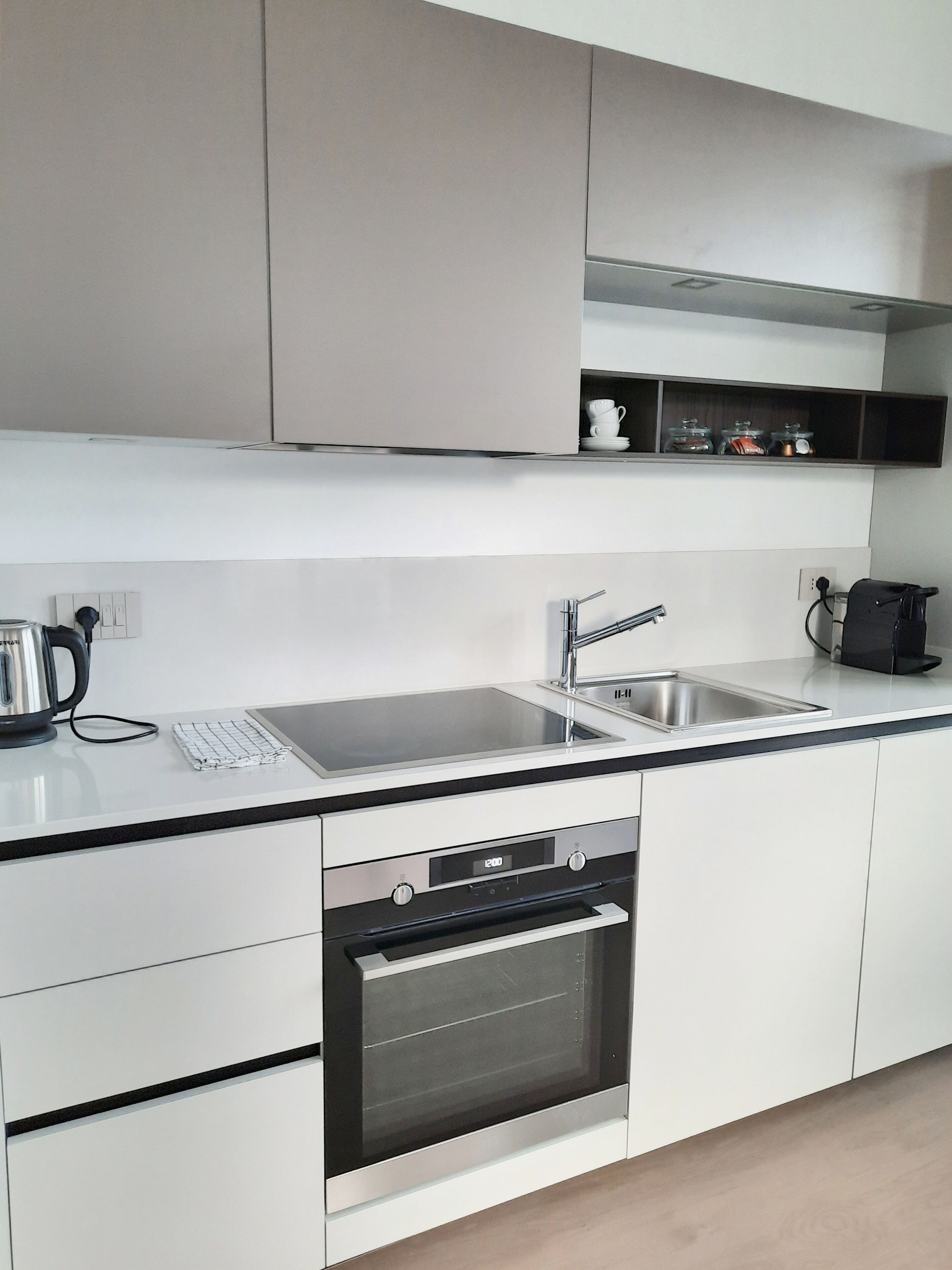 A modern kitchen with a stainless steel sink, a kettle, and a built-in oven.