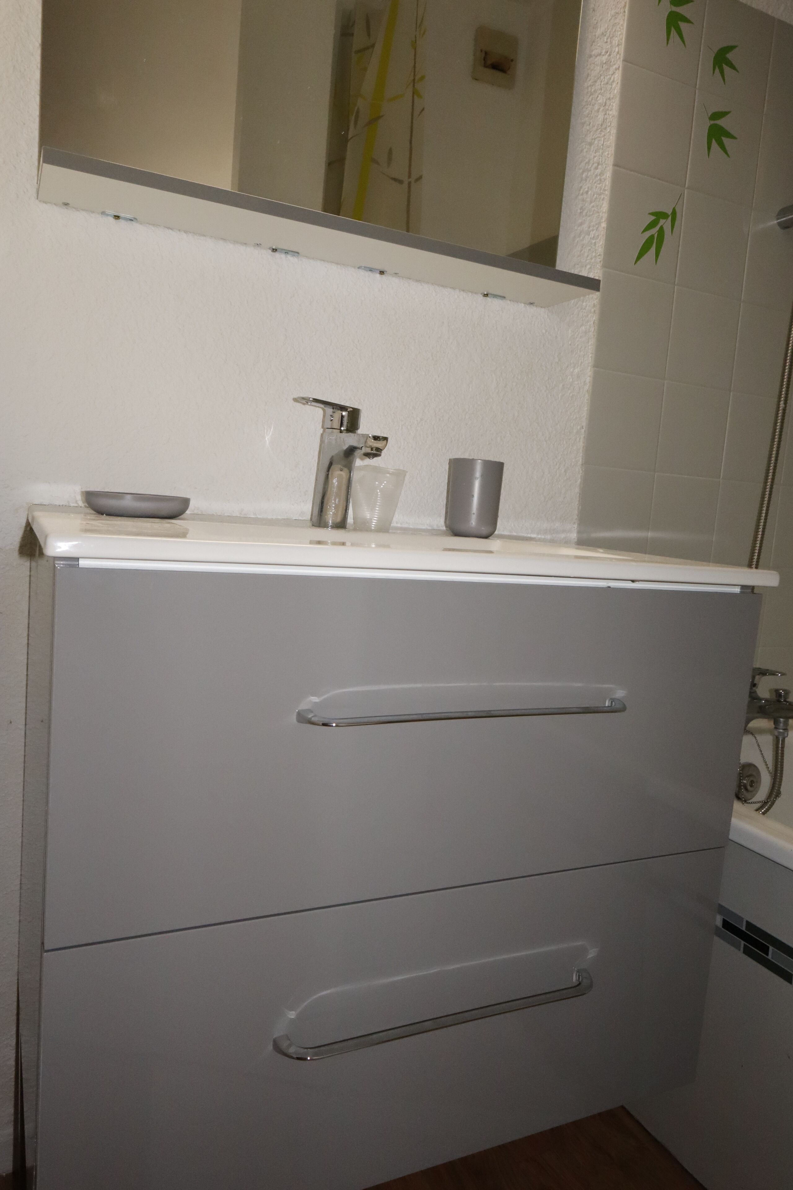A bathroom with a white vanity, a mirror, a sink, and a shower area.