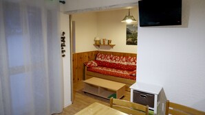 Ett litet, ombonat rum med en soffa i trä, ett litet bord och en tv som är monterad på väggen.