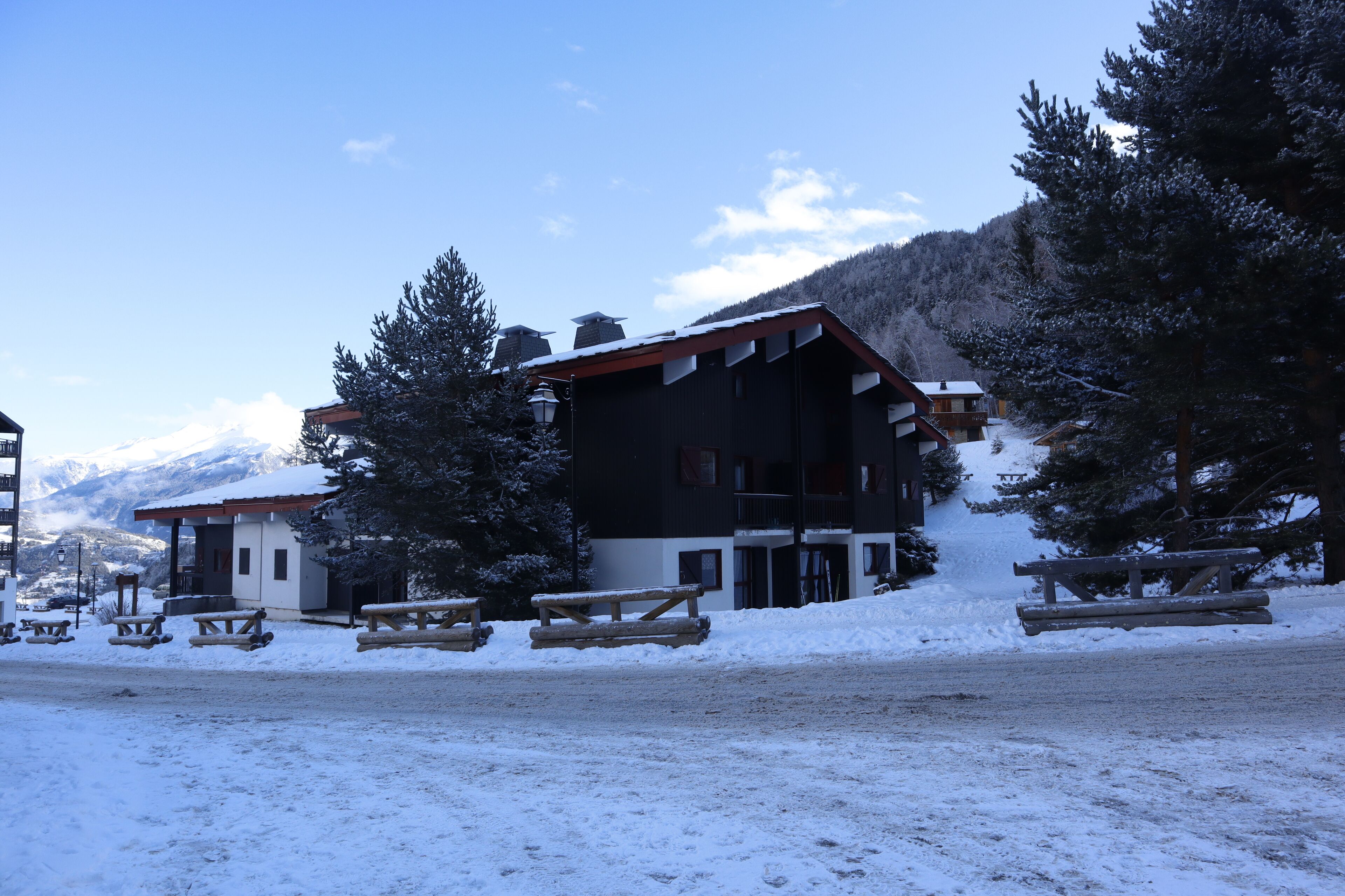 Un edificio con fachada de madera, rodeado de suelo y árboles cubiertos de nieve, bajo un cielo despejado.