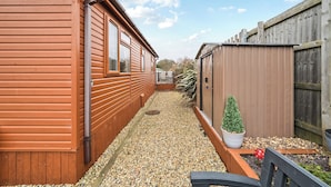 A wooden building with a gravel pathway, a small potted plant, and a red spherical object. - 2 Bed Cabin - Sleeps 4 - Pets - 5 min to Beach (Bridlington)