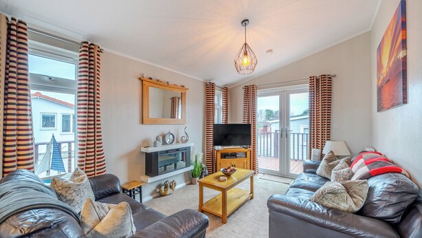A living room with a sofa, a coffee table, a TV, and a sliding glass door leading to an outdoor area. - 2 Bed Cabin - Sleeps 4 - Pets - 5 min to Beach (Bridlington)