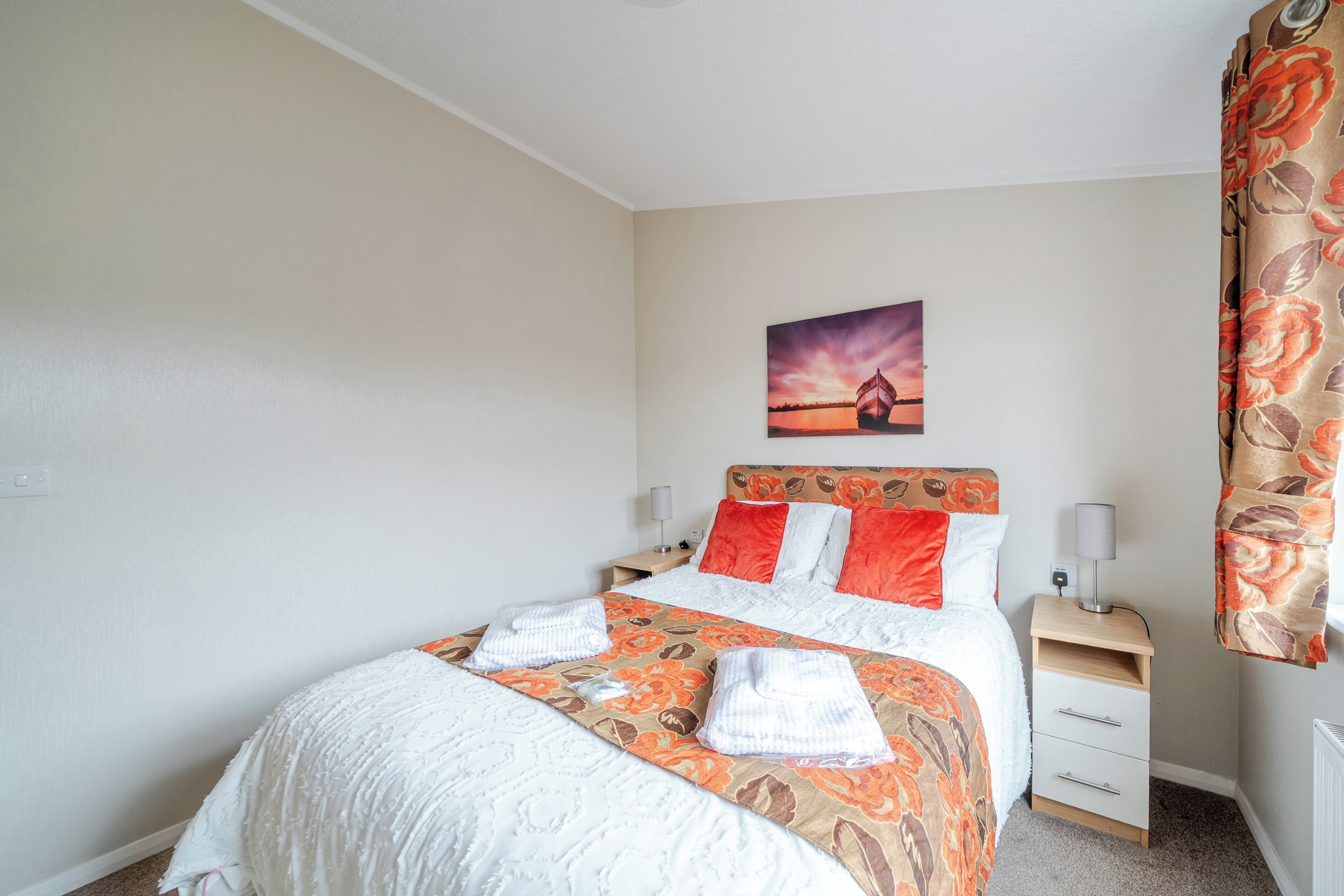A neatly made bed with a floral bedspread, a nightstand with a lamp, and a painting on the wall.