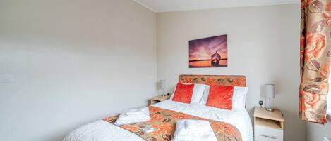 A neatly made bed with a floral bedspread, a nightstand with a lamp, and a painting on the wall.