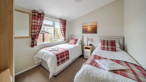 A bedroom with two beds, a window with curtains, a bedside table with a lamp, and a painting on the wall. - 2 Bed Cabin - Sleeps 4 - Pets - 5 min to Beach (Bridlington)