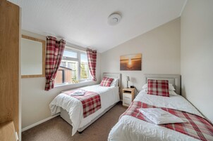 Quarto com duas camas, janela com cortinas, mesa de cabeceira com abajur e um quadro na parede.