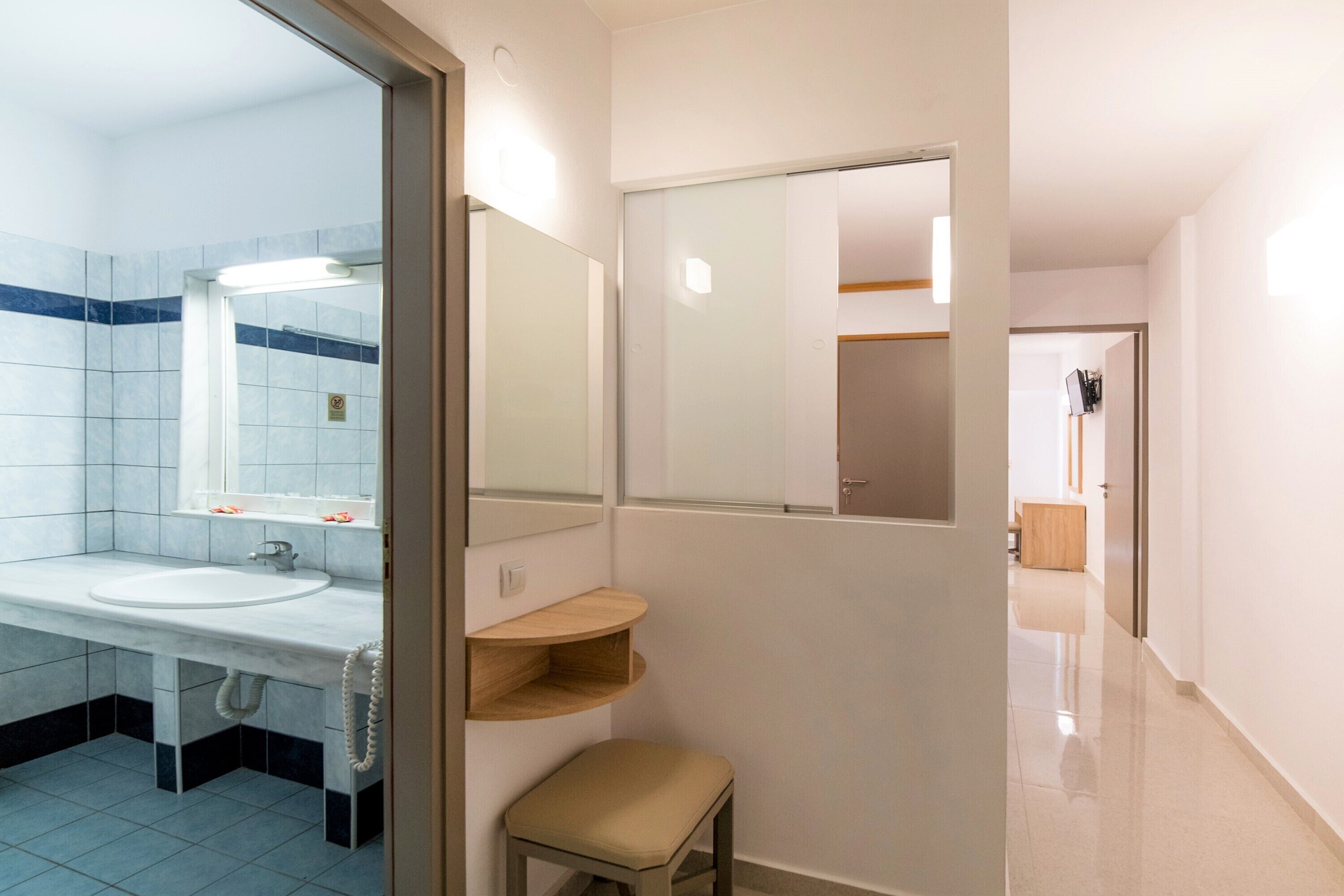 Casa de banho moderna com lavatório branco, espelho e toucador. Tem um porta-toalhas e uma prateleira com artigos de higiene pessoal.