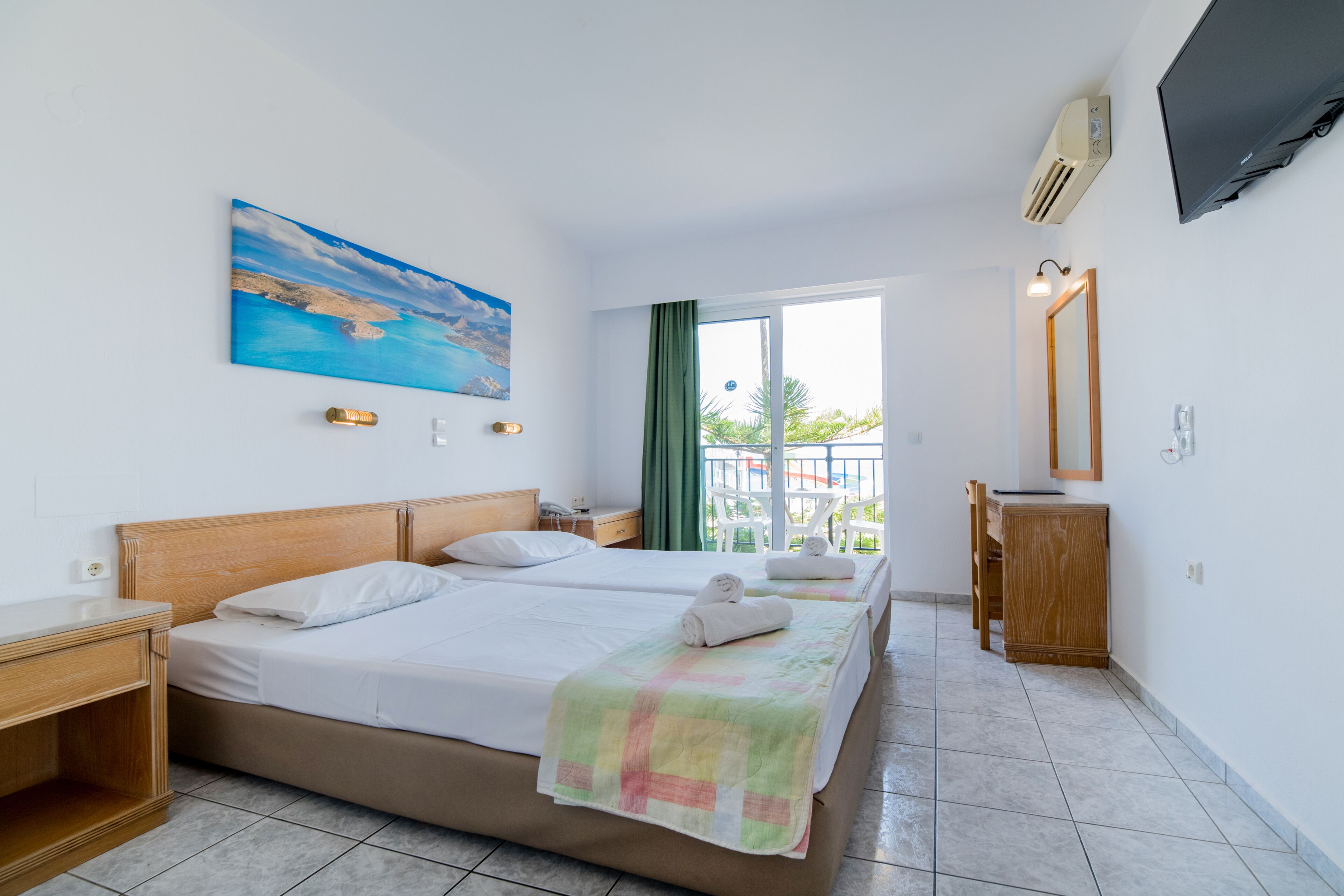 Quarto de hotel com duas camas, um quadro, uma televisão e uma varanda com vista.