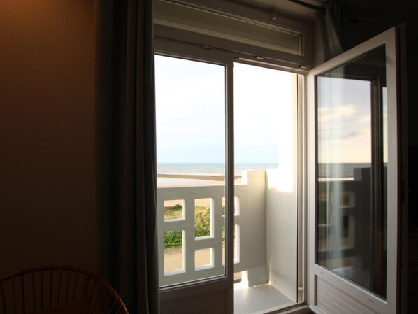 A room with a large sliding glass door leading to a balcony with a view of the beach and ocean.