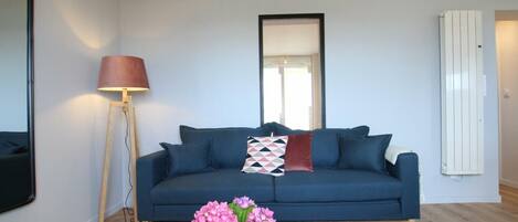 A modern living room with a blue sofa, a floor lamp, a mirror, and a radiator.