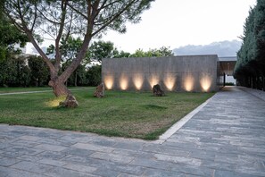 Un chemin pavé mène à un bâtiment moderne doté d’une façade en béton et de fenêtres illuminées.