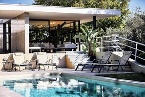 Un espace piscine extérieur moderne, doté de chaises longues et d’un coin salon abrité.