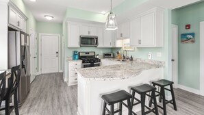 A kitchen with white cabinets, a granite countertop, a stainless steel refrigerator, a microwave, a stove, and a sink. There are two bar stools at the island.