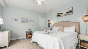 A bedroom with a bed, a nightstand, a lamp, a ceiling fan, and wall art.