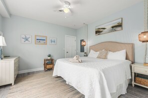 Une chambre à coucher comprenant un lit, une table de chevet, une lampe, un ventilateur de plafond et des œuvres d’art murales.