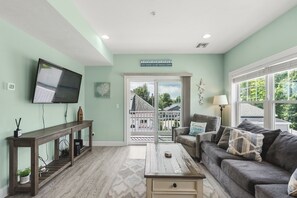A living room with a television, a sofa, a coffee table, and a view of the outside. - Beachside Abode 2B (Old Orchard Beach)