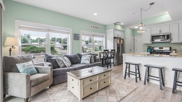 A modern kitchen with a central island, bar stools, and a dining area with a sofa and coffee table.