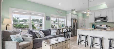 A modern kitchen with a central island, bar stools, and a dining area with a sofa and coffee table.