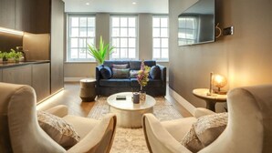 A modern living room with a sofa, armchairs, a coffee table, and a TV mounted on the wall. - Impeccable 1-bedroom Apartment in London (London)