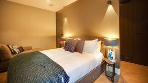 A modern hotel room with a large bed, bedside lamps, a small table with a bottle, and a couch. - Impeccable 1-bedroom Apartment in London (London)