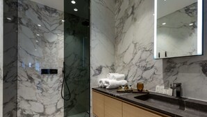 A modern bathroom with marble walls, a glass-enclosed shower, and a vanity with toiletries. - Impeccable 1-bedroom Apartment in London (London)