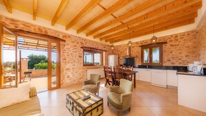 Un salón amplio con techo de madera, una mesa de comedor con sillas, un sofá y una zona de cocina con refrigerador y cafetera.