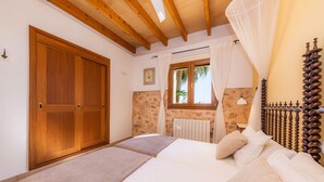 Un dormitorio con puerta de madera, ventana con cortinas, cama con ropa blanca y cabecera de madera.
