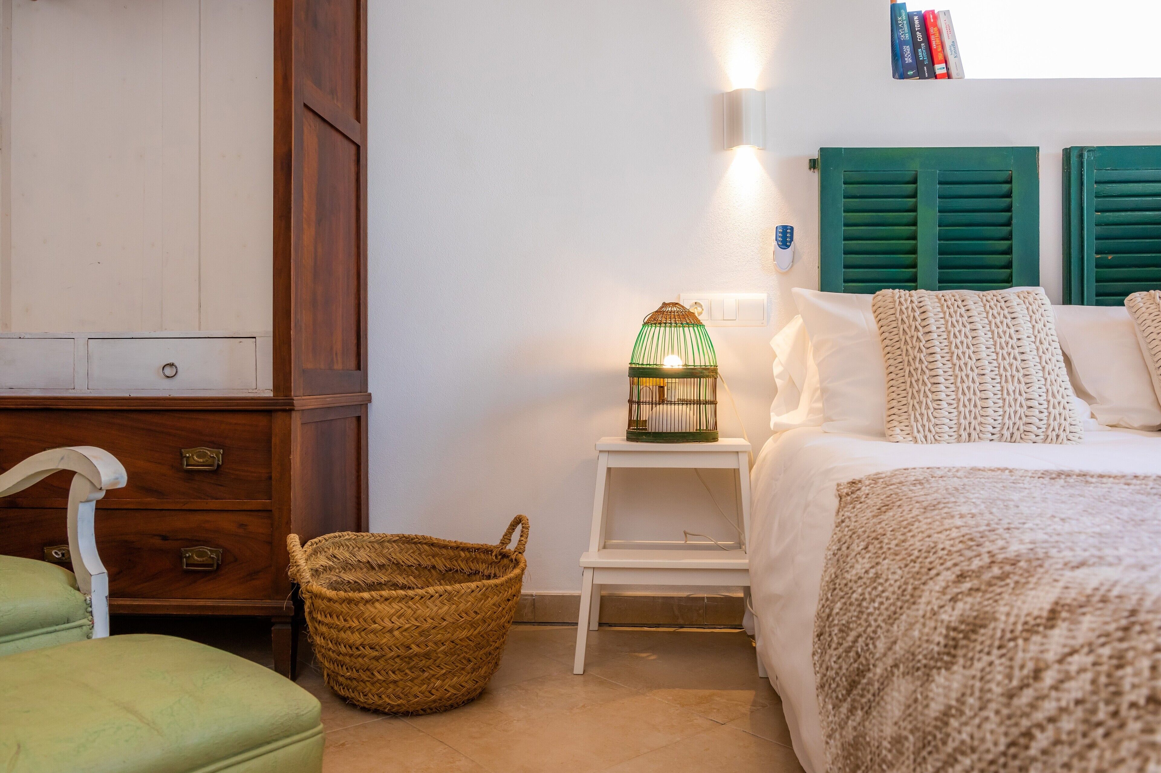 Un dormitorio con cama, mesita de noche, lámpara, cesta y cómoda.
