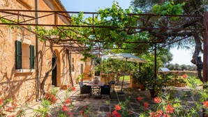 Un bâtiment rustique en pierre, agrémenté d’une pergola, d’un espace de repos extérieur et de plantes fleuries.
