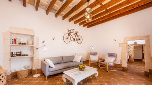 Un salon rustique avec des poutres apparentes, un canapé, des fauteuils, une table basse et un vélo suspendu au plafond.