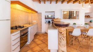 A kitchen with a gas stove, oven, white cabinets, a wooden island, and a dining area with white chairs. - Agroturismo 'Ponent' with Mountain Views, Shared Pool and Wi-Fi (Llucmajor)