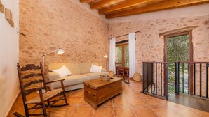 A cozy room with a wooden rocking chair, a sofa, a wooden chest, and a balcony with a metal railing. - Agroturismo 'Ponent' with Mountain Views, Shared Pool and Wi-Fi (Llucmajor)
