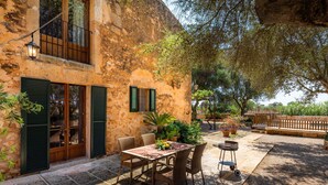 A rustic stone building with a balcony, a dining area with wicker furniture, and potted plants. - Agroturismo 'Ponent' with Mountain Views, Shared Pool and Wi-Fi (Llucmajor)