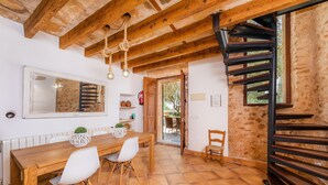 A rustic kitchen with a wooden table, white chairs, and a spiral staircase. - Agroturismo 'Ponent' with Mountain Views, Shared Pool and Wi-Fi (Llucmajor)