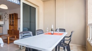 Zona pranzo con tavolo bianco, sedie nere e una bottiglia di vino.