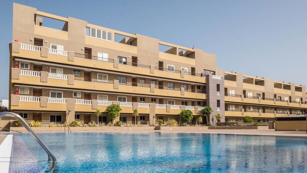 Un hotel a più piani con balconi, una piscina e un cielo sereno.