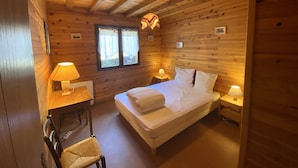 Een gezellig houten kamer met een bed, twee bedlampen, een klein tafeltje en een stoel.