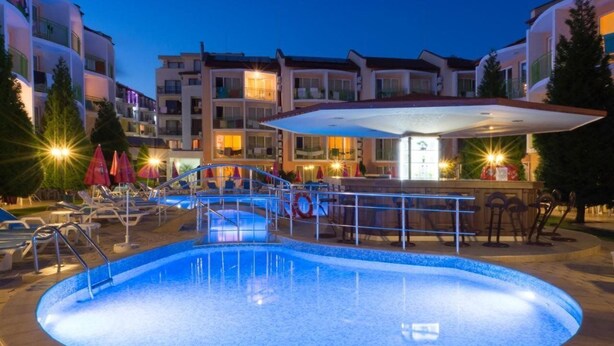 A swimming pool with a sunken center, surrounded by lounge chairs and umbrellas, with a bar area and multi-story buildings in the background. - Sun City Hotel (Sunny Beach)